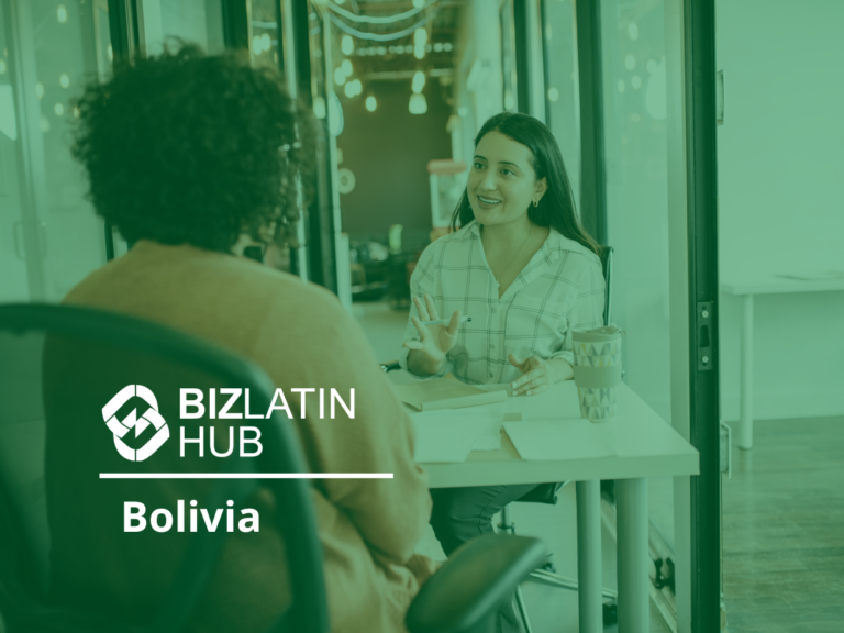 Two people sitting at a desk and having a conversation in an office setting. The person facing the camera is wearing a checkered shirt, and the person with their back to the camera has curly hair. A logo for BizLatin Hub with the text "Bolivia" is visible in the foreground, discussing tipos de visto na Colômbia.