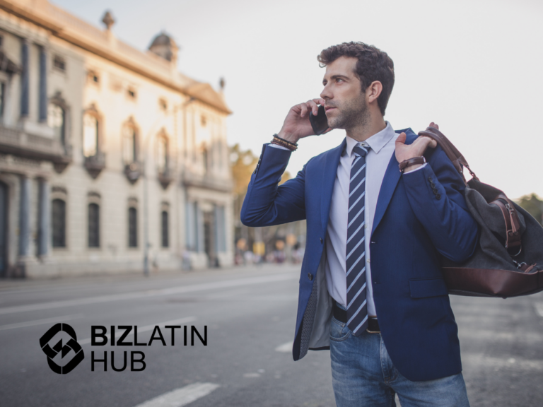 A man in a blue jacket and striped tie is standing on a street, talking on his phone while holding a bag over his shoulder. He is in an urban area with buildings in the background, possibly discussing the upcoming presidential elections in Guatemala. The "BIZLATIN HUB" logo is visible in the bottom left corner of the image.