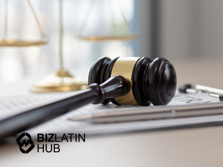 A wooden gavel rests on a white desk near some documents and a silver pen, symbolizing legal matters possibly linked to nearshoring in Panama. In the background, a scale symbolizing justice is slightly blurred. The "BizLatin Hub" logo is visible in the bottom left corner.