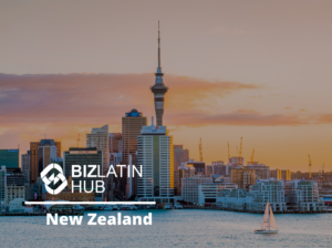 Sunset view of Auckland, New Zealand's skyline featuring the Sky Tower and several buildings with a sailboat in the foreground. The BizLatin Hub logo and the text "New Zealand" are overlaid on the image, touching on topics like tipos de visto na Colômbia.