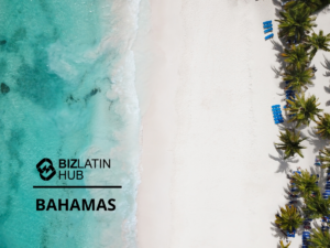 Aerial view of a beach with clear turquoise water on the left and white sand on the right. There are several blue beach chairs lined up under palm trees at the top right of the image. The logo of BizLatin Hub and the word "Bahamas" are placed on the left side of the photo.