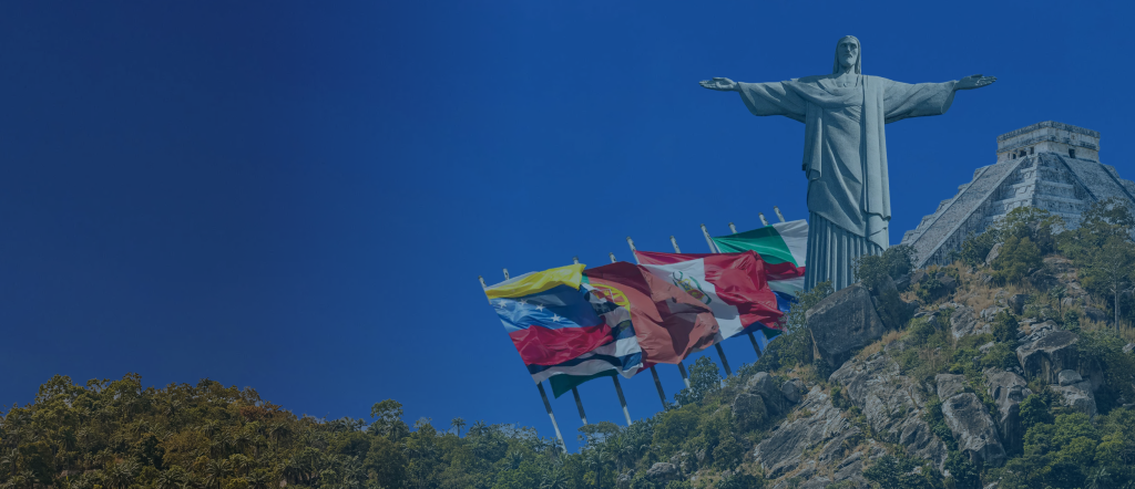 Una gran estatua del Cristo Redentor se alza sobre una colina rocosa, rodeada de vegetación. A la izquierda de la estatua se ven varias banderas nacionales, entre ellas las de Venezuela, Perú, Brasil y Argentina. El cielo azul despejado enmarca perfectamente este emblemático monumento en su pintoresco entorno.  

